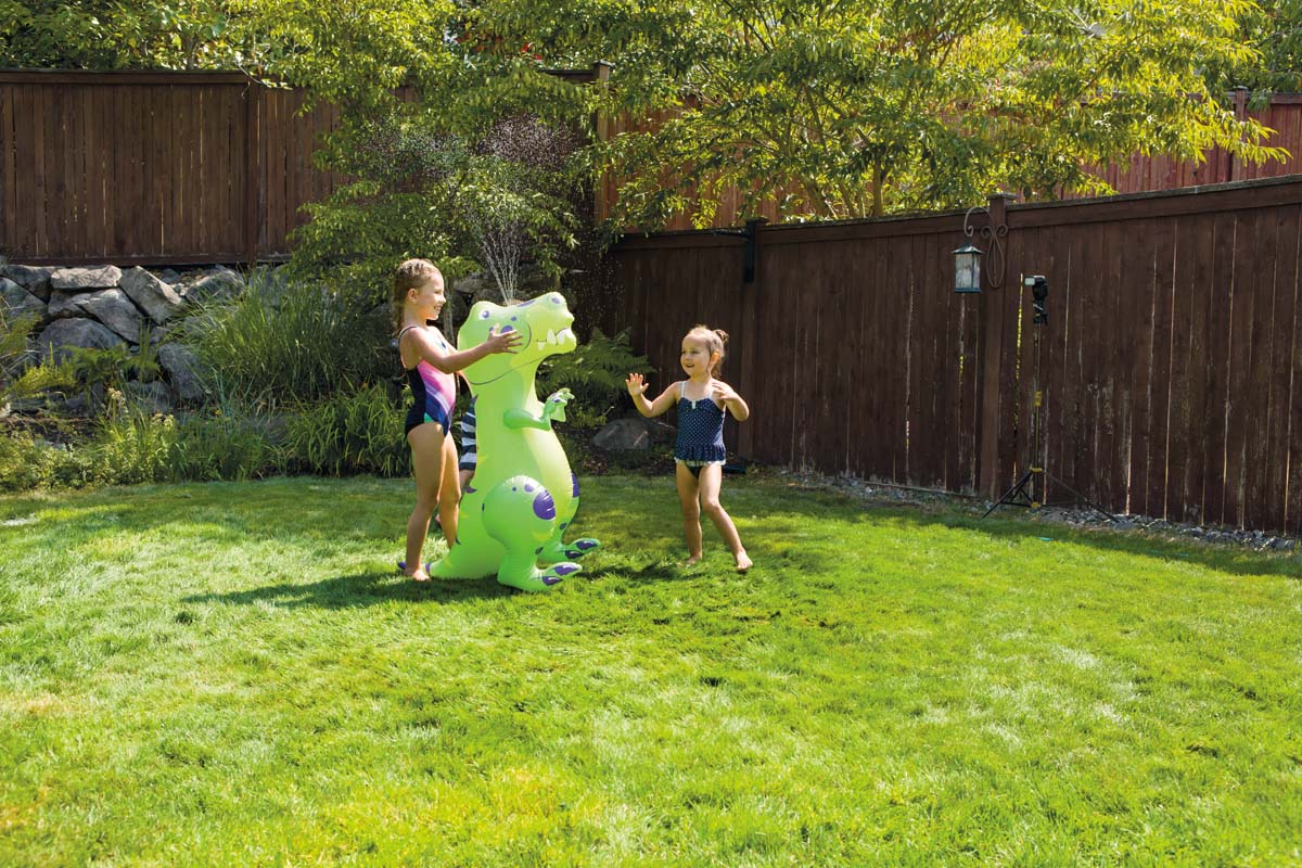Two girls playing outside with the dinosaur sprinkler