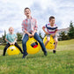 Three children cheerfully bouncing on Happy Hoppy Balls outside.