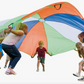 Children running inwardly in a circle holding the handles of a color-blocked parachute.